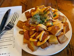 El Raval signature dishes Pan con Tomate, Patatas Bravas, and a selection of Spanish hams and cheeses.